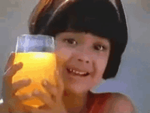 a young girl is holding a glass of orange juice in her hand .