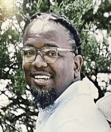 a man with glasses and a beard is smiling in front of a tree