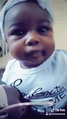 a baby girl wearing a headband is making a funny face while looking at the camera .