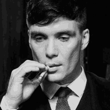 a man in a suit and tie smoking a cigarette in a black and white photo