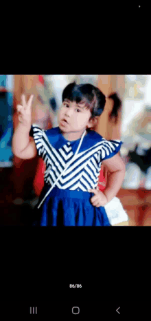 a little girl in a blue and white striped dress is giving the peace sign