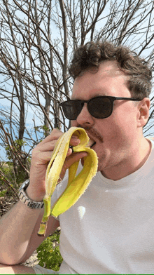 a man wearing sunglasses eating a banana outside