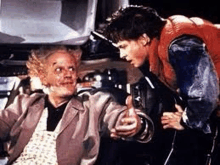 a man in a red vest is giving a thumbs up to a man in a suit in back to the future .