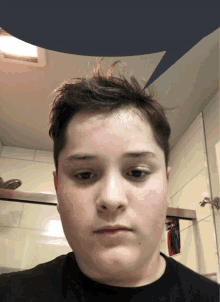 a young man in a black shirt looks at the camera in a bathroom