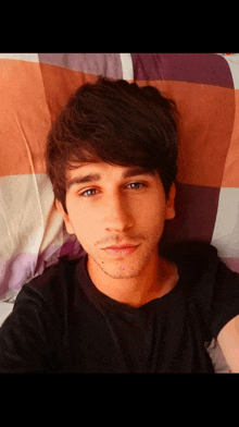 a young man is laying on a bed with a plaid blanket