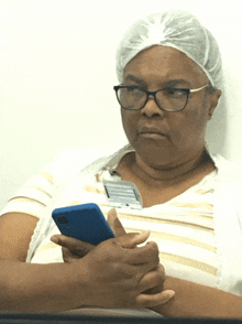 a woman wearing glasses and a name tag holds a cellphone