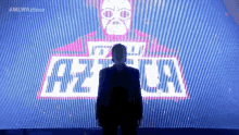 a man in a suit stands in front of a screen with the word azteca on it