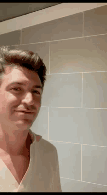 a man in a white shirt is standing in front of a tiled wall and smiling