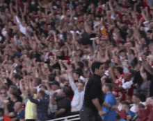 a man in a black shirt stands in front of a crowd of people with their arms in the air