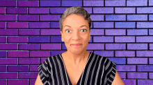 a woman is making a funny face in front of a brick wall