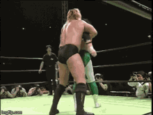 two wrestlers are fighting in a wrestling ring with a referee watching .