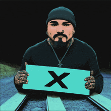 a man with a beard is holding a sign that has the letter x on it