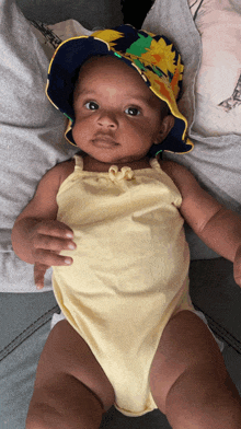 a baby wearing a hat and a yellow bodysuit is laying on a couch