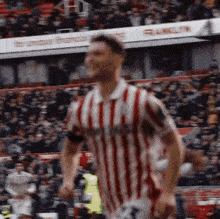 a man in a red and white striped shirt is running on a soccer field in front of a crowd