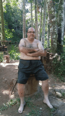 a man without a shirt is sitting on a stump in the woods