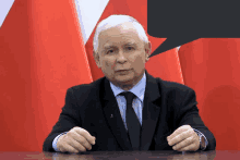 a man in a suit and tie is sitting at a table with a speech bubble behind him