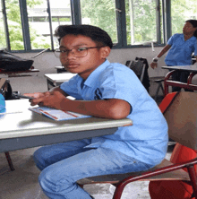 a boy in a blue shirt with the letter s on the front sits at a desk in a classroom