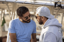 two men wearing sunglasses and hats are looking at each other with a camera behind them that says serg photography