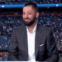 a man in a suit is sitting in front of a crowd in a stadium with a sign that says vs.