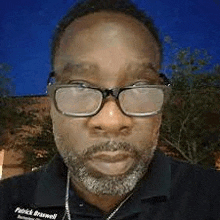 a man with glasses and a beard is standing in front of a building .