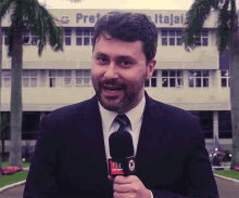 a man in a suit and tie is holding a microphone in front of a building that has the word prefeitura on it