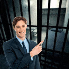 a man in a suit and tie points to a cell in a jail