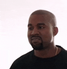 kanye west is wearing a black shirt and a necklace and looking at the camera .