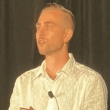 a man in a white shirt is standing in front of a microphone and giving a speech .