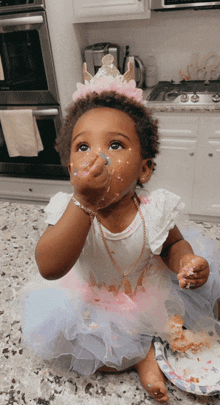 a little girl wearing a tiara is eating cake