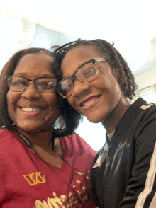 a woman wearing a red shirt with the letter w on it stands next to a young girl wearing glasses