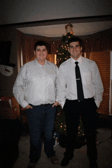 two men stand in front of a christmas tree