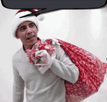 a man wearing a santa hat is carrying a bag of christmas presents