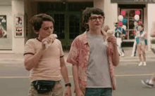 two young boys are eating ice cream cones on the side of the road .