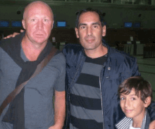 three men posing for a picture with one wearing a black jacket