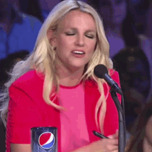 a woman in a pink shirt is sitting in front of a microphone next to a cup of pepsi .