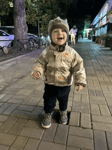 a little boy wearing a camouflage jacket and a hat is standing on a sidewalk