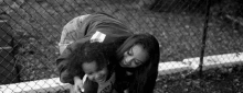 a woman is piggybacking a little girl in front of a chain link fence in a black and white photo .