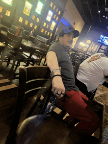 a man in a hat sits at a table in a restaurant with a white shirt with the letter f on it