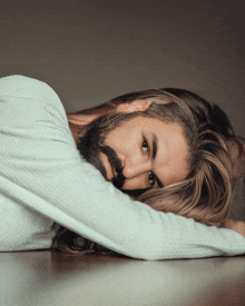 a man with long hair and a beard rests his head on his arms