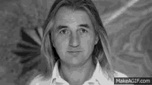 a man with long hair is wearing a white shirt and looking at the camera .