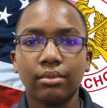 a young man wearing glasses stands in front of an american flag and a cho logo