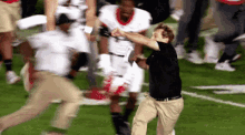 a man in a black shirt and khaki pants is running on a football field with a crowd of people behind him .