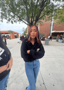 a girl in a black sweater and blue jeans stands in front of a tree