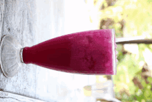 a purple smoothie in a clear glass on a wooden table