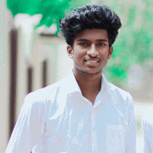 a young man wearing a white shirt is smiling and looking at the camera