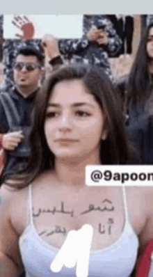 a woman wearing a white tank top with arabic writing on her chest .