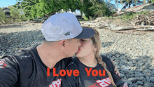 a man and woman kissing on a rocky beach with the words i love you in red