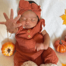 a baby wearing orange overalls and a headband is laying on a bed