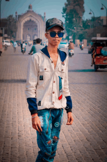 a young man wearing sunglasses and a hat stands on a brick street