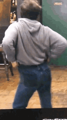 a man in a grey hoodie and jeans is dancing in front of a green door